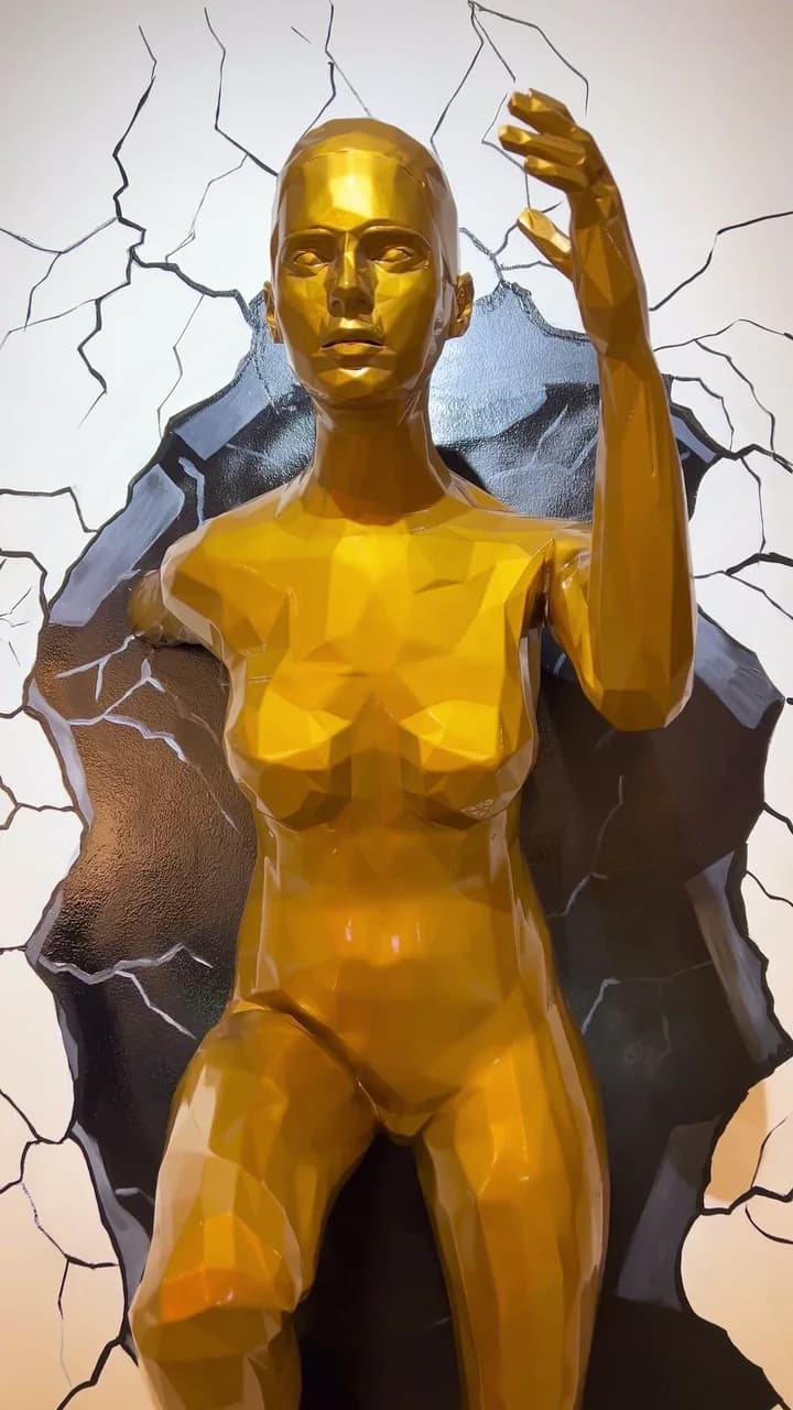 Close to the figure: the face, the raised hand and the low-poly facets in metallic gold.