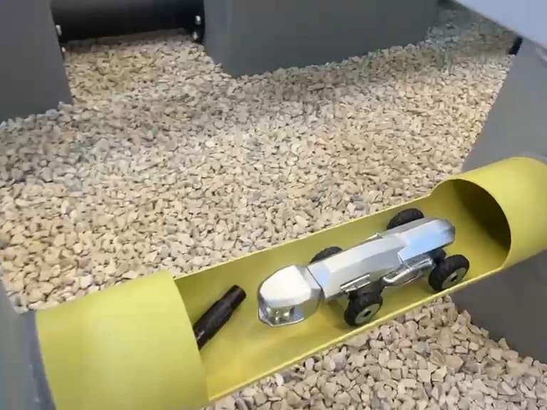 روبوت فحص داخل أنبوب أصفر مفتوح بالقطع على طوله، في الحصى.